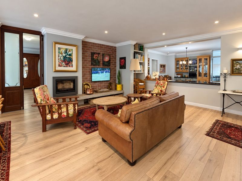 Spacious open-plan living area featuring a cozy brick fireplace, modern laminate flooring, and a seamless transition to the kitchen with a breakfast bar.