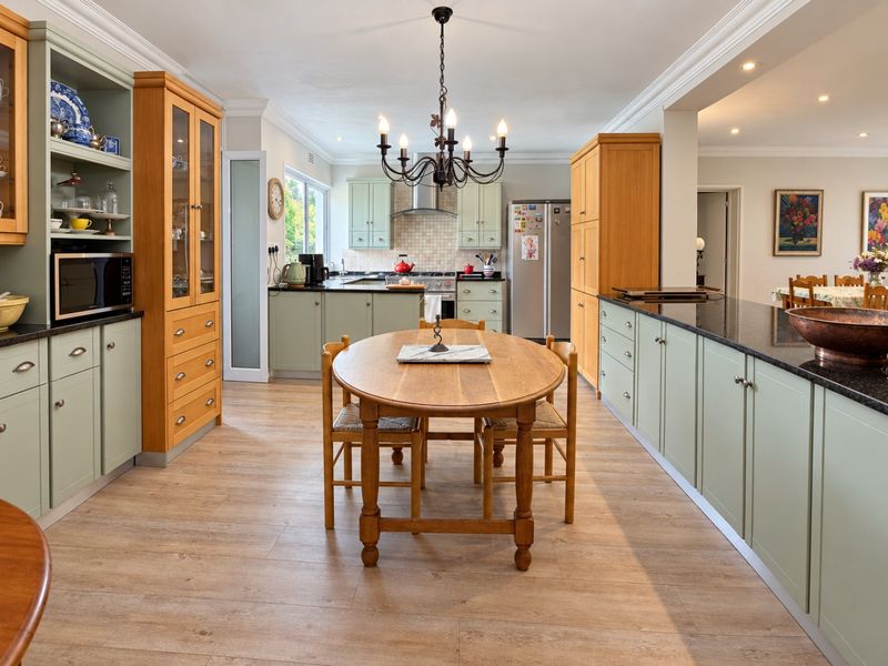 Spacious kitchen featuring sage green and natural wood cabinetry, granite countertops, integrated appliances, and a central dining area with elegant chandelier lighting.