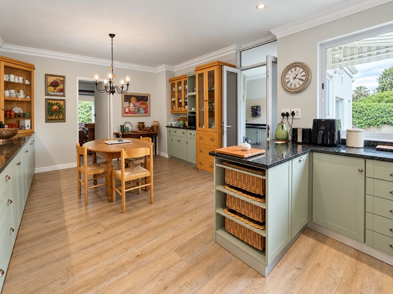 Spacious kitchen featuring light green and timber cabinetry, granite countertops, laminate flooring, and integrated storage solutions with a dedicated dining area.