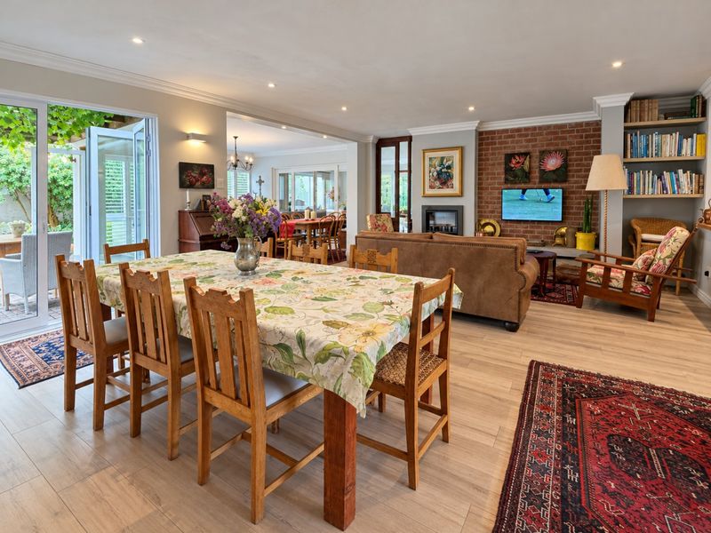 Spacious open-plan living and dining area featuring exposed brick fireplace, built-in shelving, and seamless access to the outdoor patio through bi-fold glass doors.