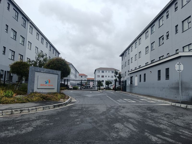 The entrance to Belhar Views complex featuring a paved driveway, security gate, and multi-story residential apartment blocks.