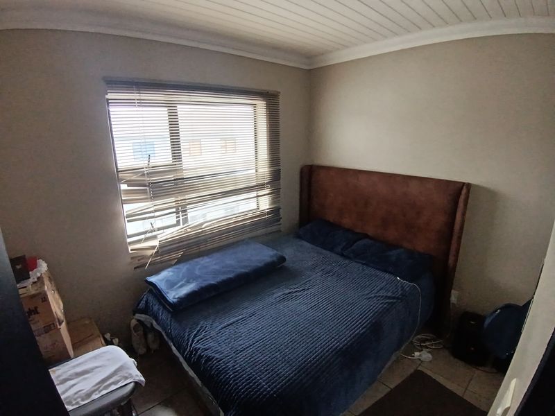 A compact bedroom featuring tiled flooring, a tongue and groove ceiling, and a window fitted with venetian blinds.