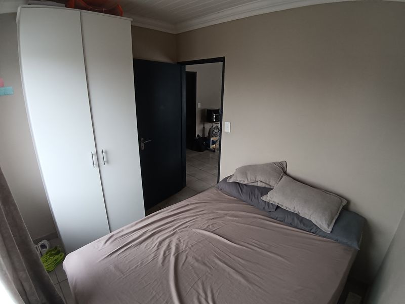A compact bedroom featuring tiled flooring, a built-in wardrobe, and neutral wall tones, providing a functional living space.