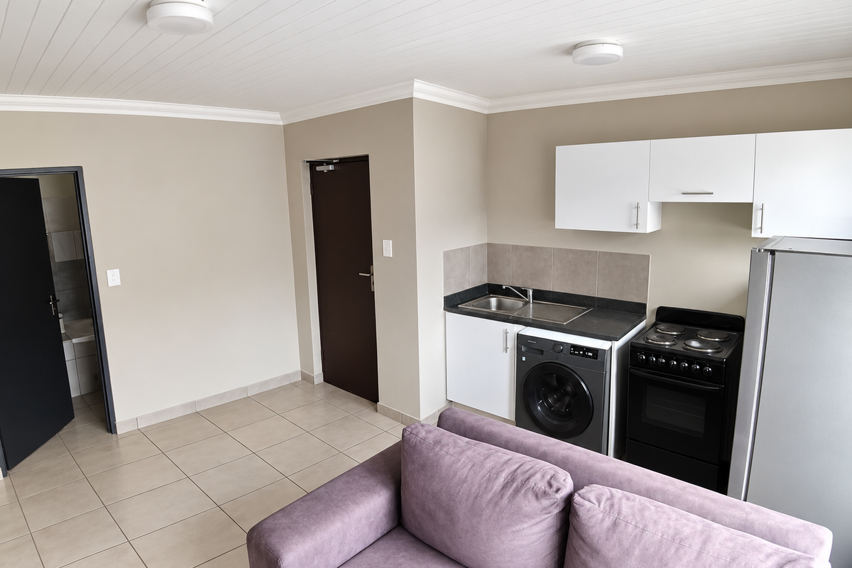Open-plan living area featuring a compact kitchen with built-in cabinetry, stove, and integrated laundry facilities, finished with neutral tones and tiled flooring.