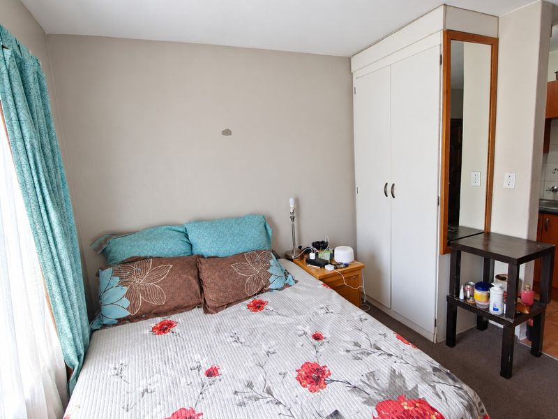 A bedroom featuring a built-in wardrobe with an integrated mirror, adjacent to a compact kitchen area with wooden cabinetry and tiled flooring.
