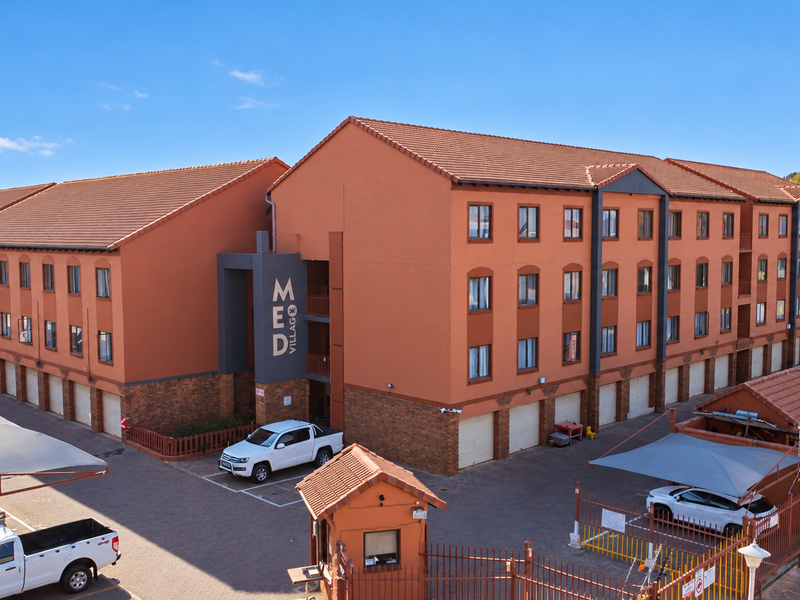 Exterior view of a multi-story apartment complex featuring brick and rendered facade, tiled roofing, and dedicated carport parking areas.