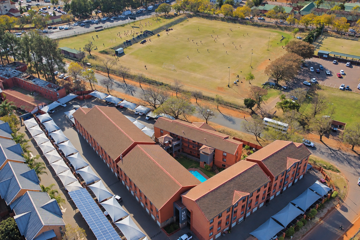 Aerial view of the apartment complex featuring multiple residential blocks, covered parking with solar panels, and a central swimming pool area.
