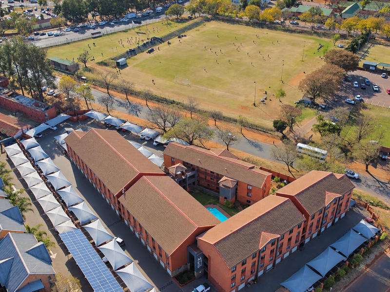 Aerial view of the apartment complex featuring multiple residential blocks, covered parking with solar panels, and a central swimming pool area.