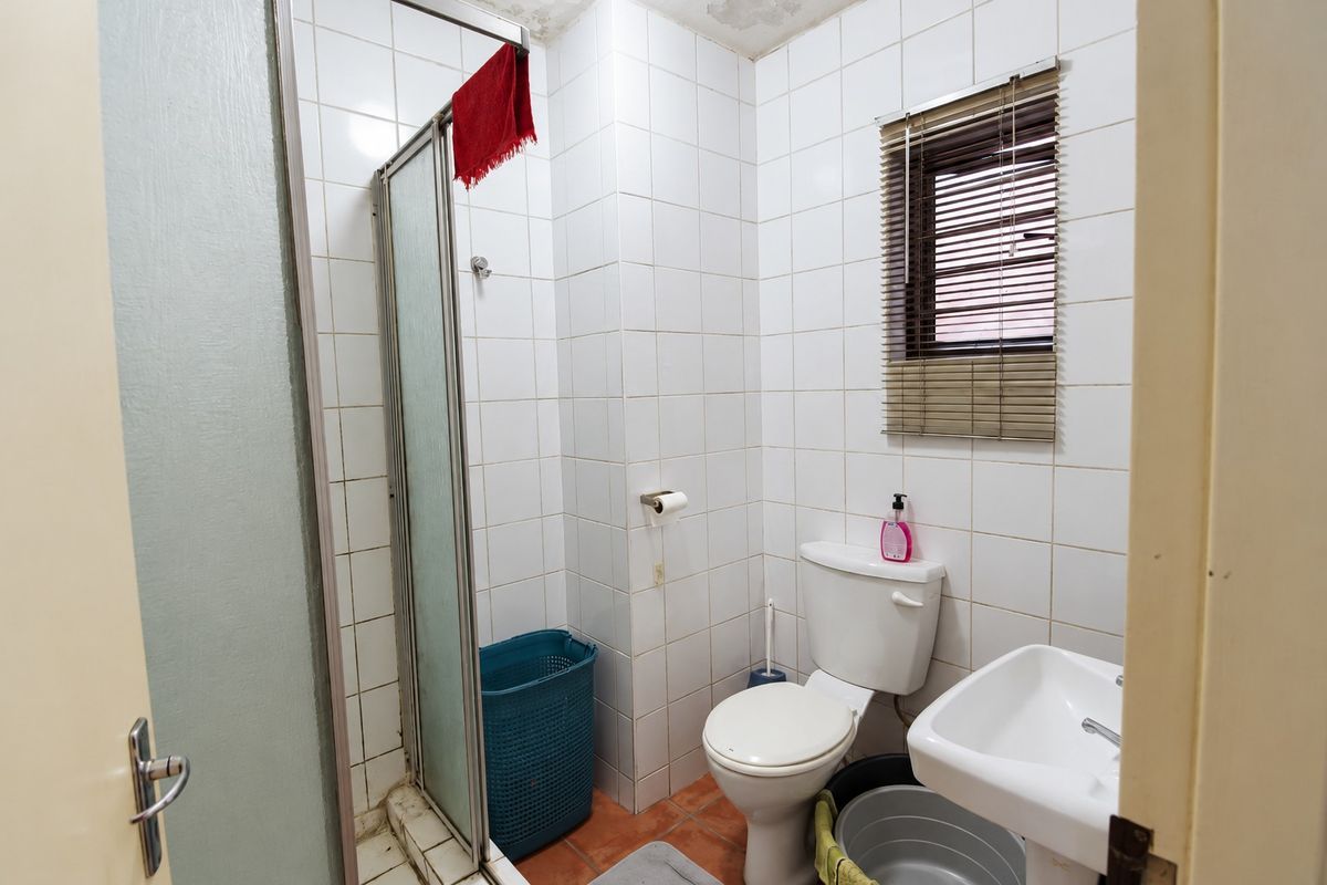 A compact bathroom featuring a shower enclosure, pedestal basin, and toilet, with white wall tiling and terracotta floor tiles. Requires cosmetic updates.