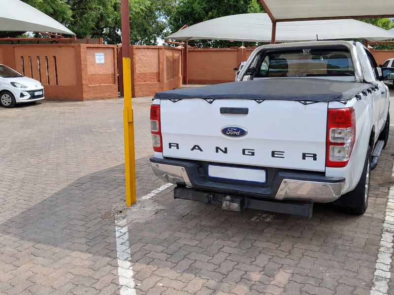 Outdoor parking area featuring paved ground and shade cloth carports within a secure perimeter wall.