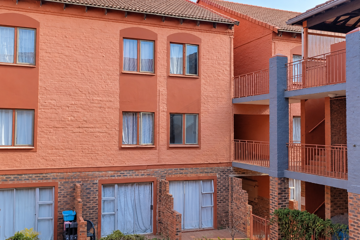 Rear view of a multi-story apartment complex featuring brick facade, metal balcony railings, and sliding glass doors.