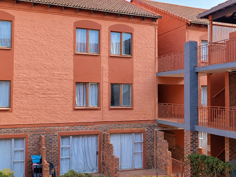 Rear view of a multi-story apartment complex featuring brick facade, metal balcony railings, and sliding glass doors.