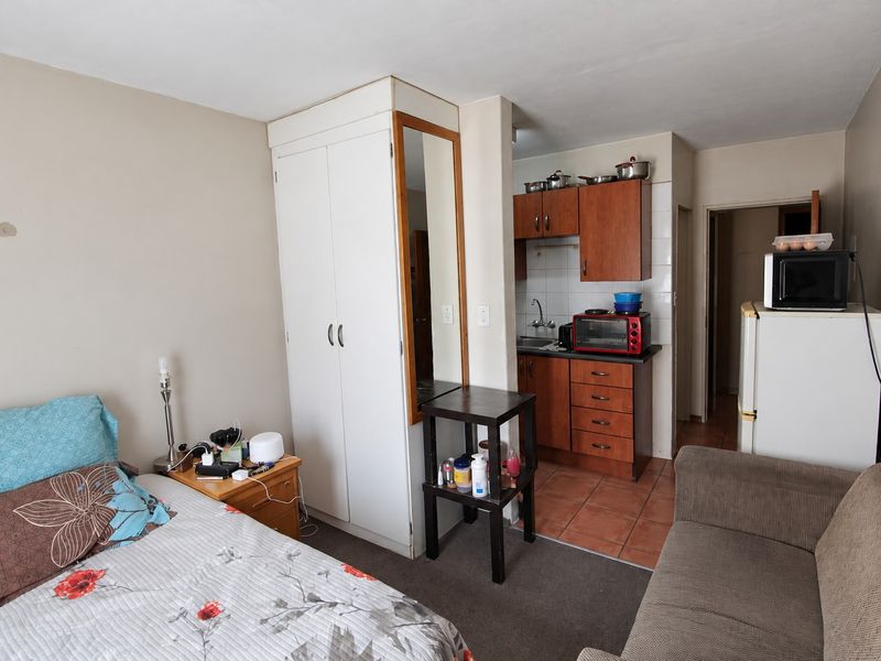 Open-plan studio apartment featuring a compact kitchenette with wooden cabinetry and a built-in wardrobe, offering a functional living and sleeping space.