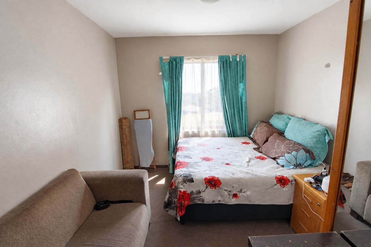 A functional bedroom featuring carpeted flooring and a window with curtains, providing a neutral space ready for personalization.