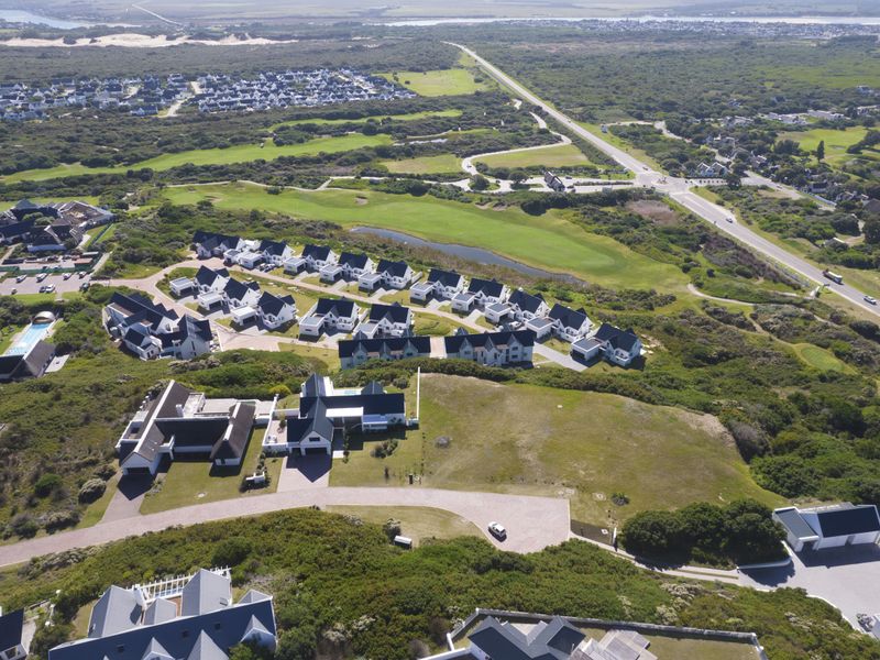 An aerial view of a residential townhouse estate situated near a golf course and coastal landscape.