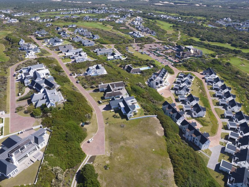 An aerial view of a residential townhouse estate featuring paved roads, landscaped grounds, and multiple housing clusters within a coastal environment.