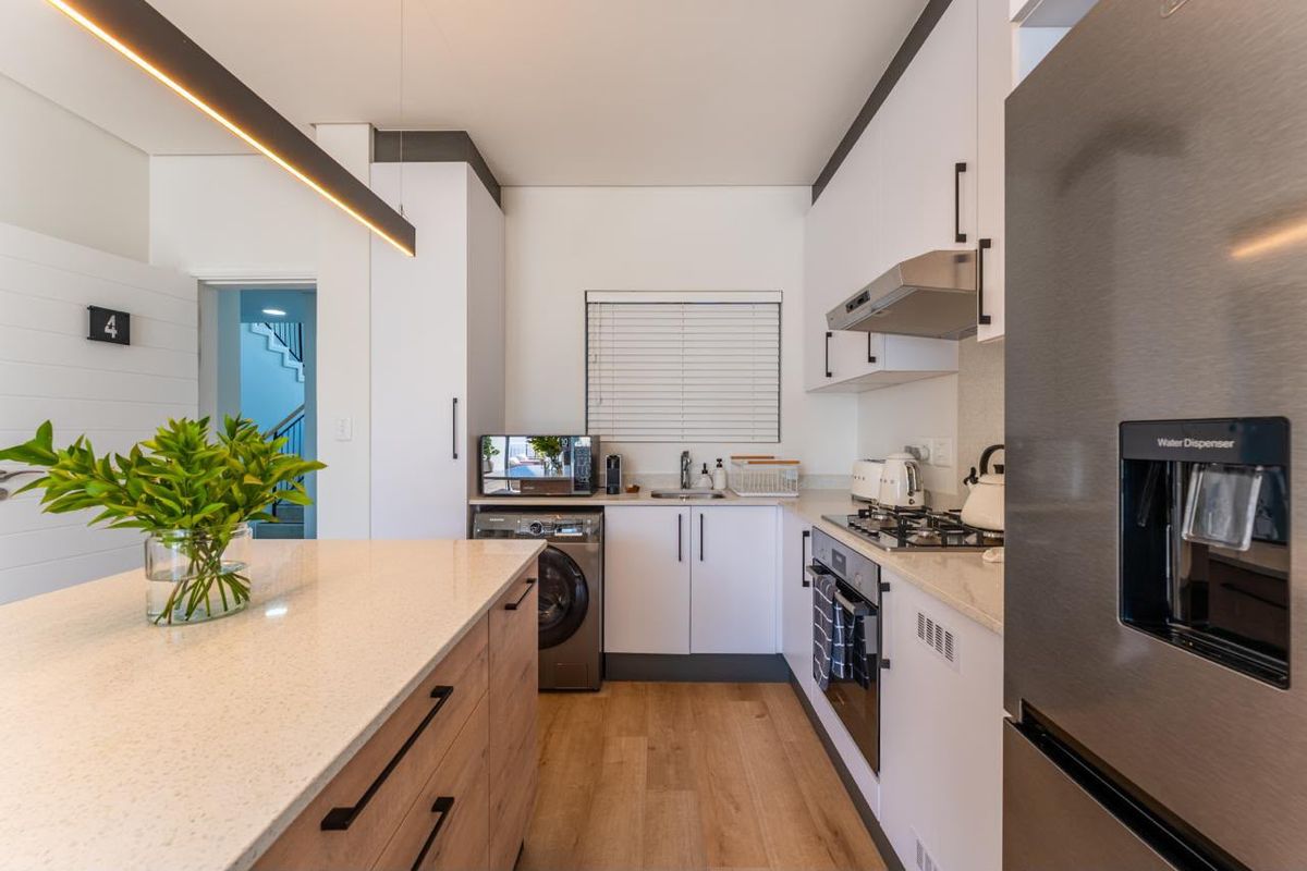 Modern kitchen featuring stone countertops, built-in oven, gas hob, extractor fan, and sleek cabinetry with integrated appliances and wood-look flooring.
