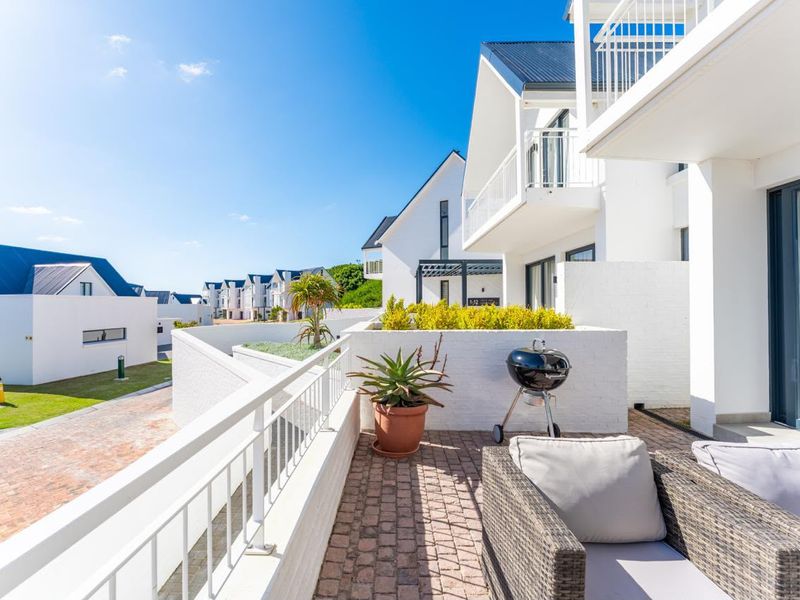 A bright, well-maintained balcony featuring brick paving, a metal balustrade, and a built-in planter box, overlooking the townhouse complex grounds.
