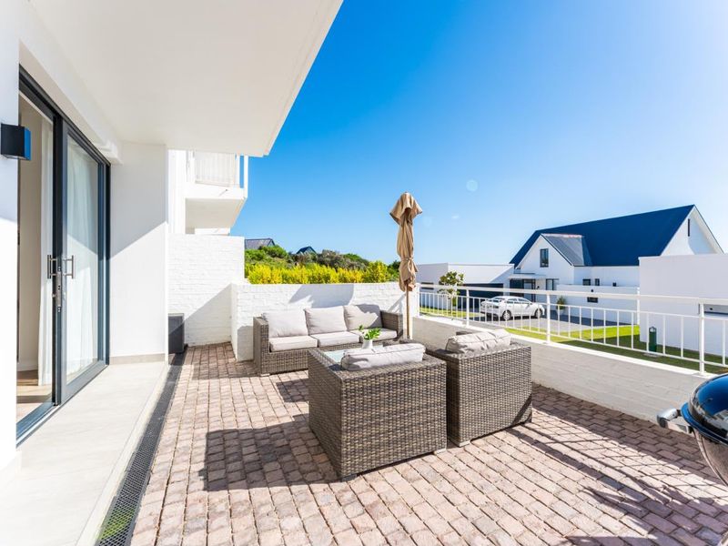 A spacious outdoor patio featuring paved flooring, white brick walls, and a metal railing, providing a pleasant area for relaxation.
