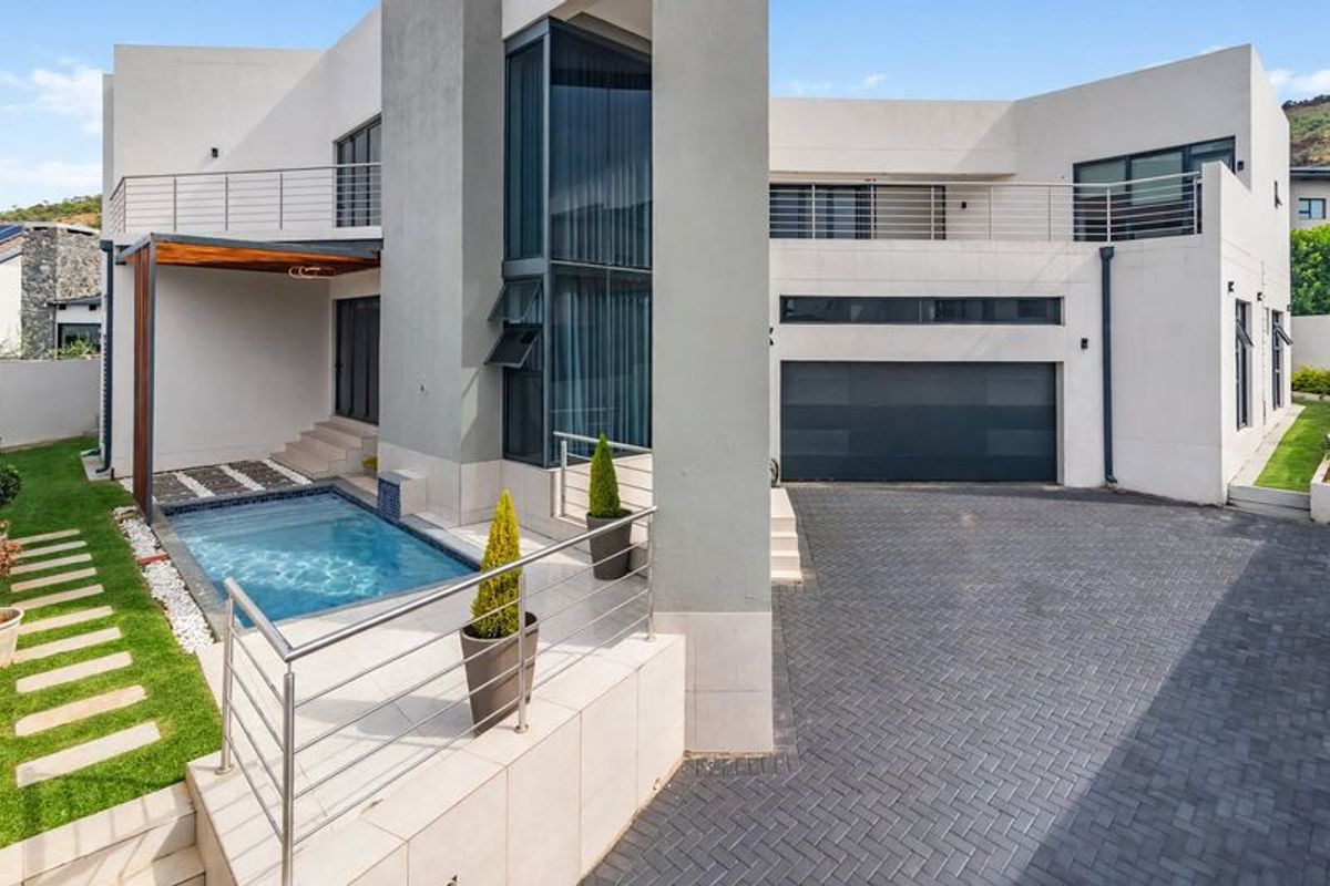 Modern rear exterior featuring a paved driveway, double garage, swimming pool, and elevated balcony with stainless steel balustrades.