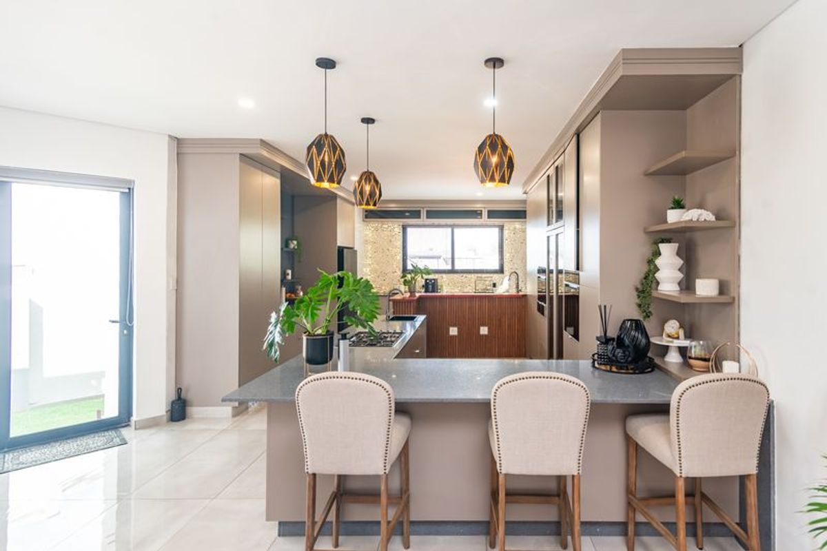 Modern kitchen featuring stone countertops, built-in cabinetry, gas hob, integrated oven, and stylish pendant lighting with a breakfast bar area.