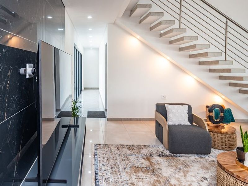 Modern living area featuring a striking floating staircase with metal balustrade, polished tiled flooring, and a sleek marble-effect feature wall.