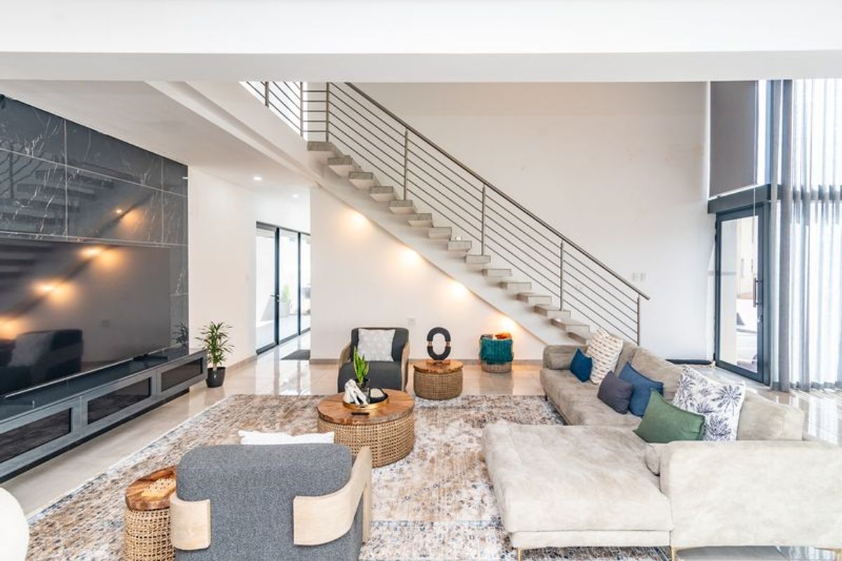 Spacious modern living room featuring a striking floating staircase, marble-look feature wall, and large glass doors providing ample natural light.