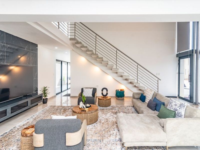 Spacious modern living room featuring a striking floating staircase, marble-look feature wall, and large glass doors providing ample natural light.