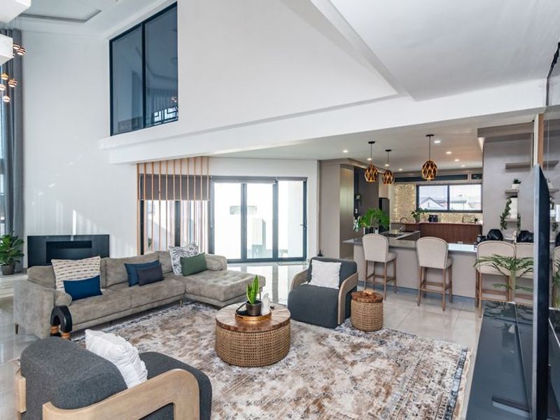 Spacious open-plan living area featuring a modern kitchen with island, double-volume ceilings, and seamless flow to the outdoor patio through large sliding doors.