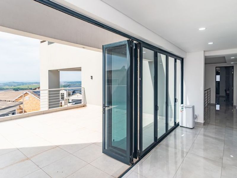 A modern, spacious balcony featuring large aluminium stacker doors, sleek tiled flooring, and a metal balustrade with expansive views.