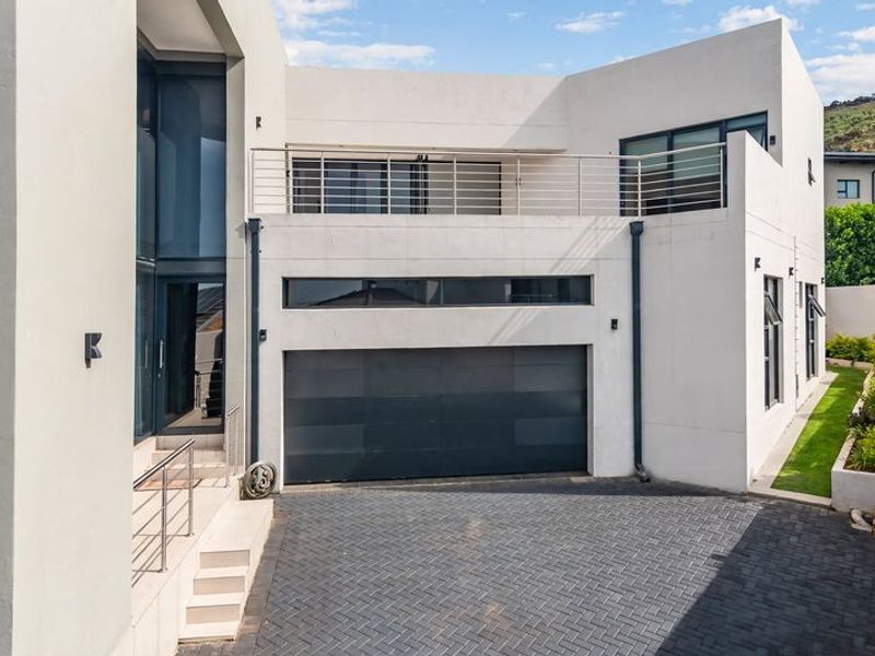 Modern architectural front elevation featuring a double garage, paved driveway, and an upper-level balcony with clean lines and contemporary finishes.
