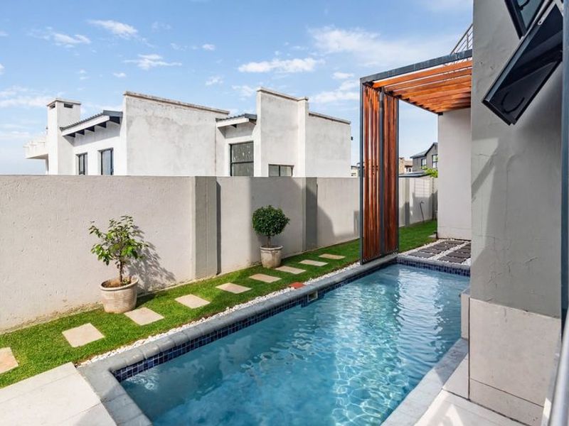 A modern outdoor pool area featuring a compact swimming pool, timber pergola structure, and a well-maintained lawn with stone pathway.