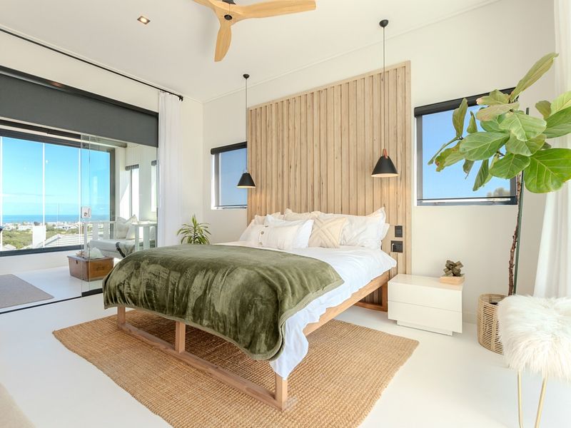 Modern bedroom featuring a timber slat feature wall, ceiling fan, and large sliding glass doors opening to a balcony with scenic views.