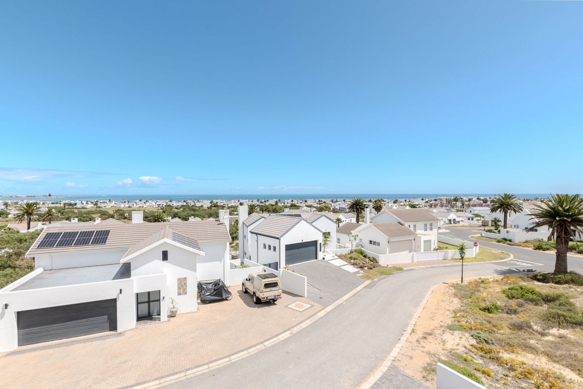 An elevated aerial view of a modern residential property featuring a paved driveway, solar panels, and a coastal neighborhood setting.