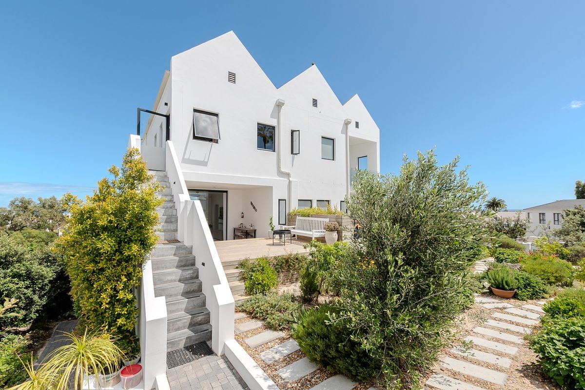 Rear view of a modern multi-level home featuring a white facade, external staircase, timber deck, and landscaped garden with paved walkways.