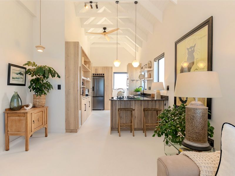 A bright open-plan living and kitchen area featuring vaulted ceilings with exposed rafters, modern light wood cabinetry, and a functional kitchen island.