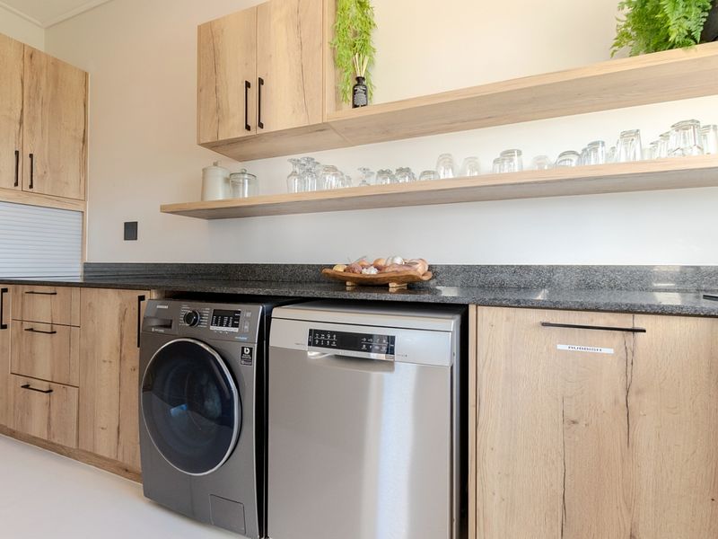 Modern laundry area featuring light wood cabinetry, stone countertops, floating shelving, and integrated appliances for a clean, functional workspace.