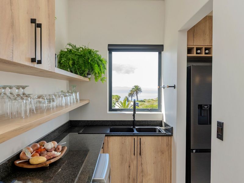 Modern scullery featuring wood-finish cabinetry, granite countertops, a double sink, and open shelving, with a window offering scenic coastal views.