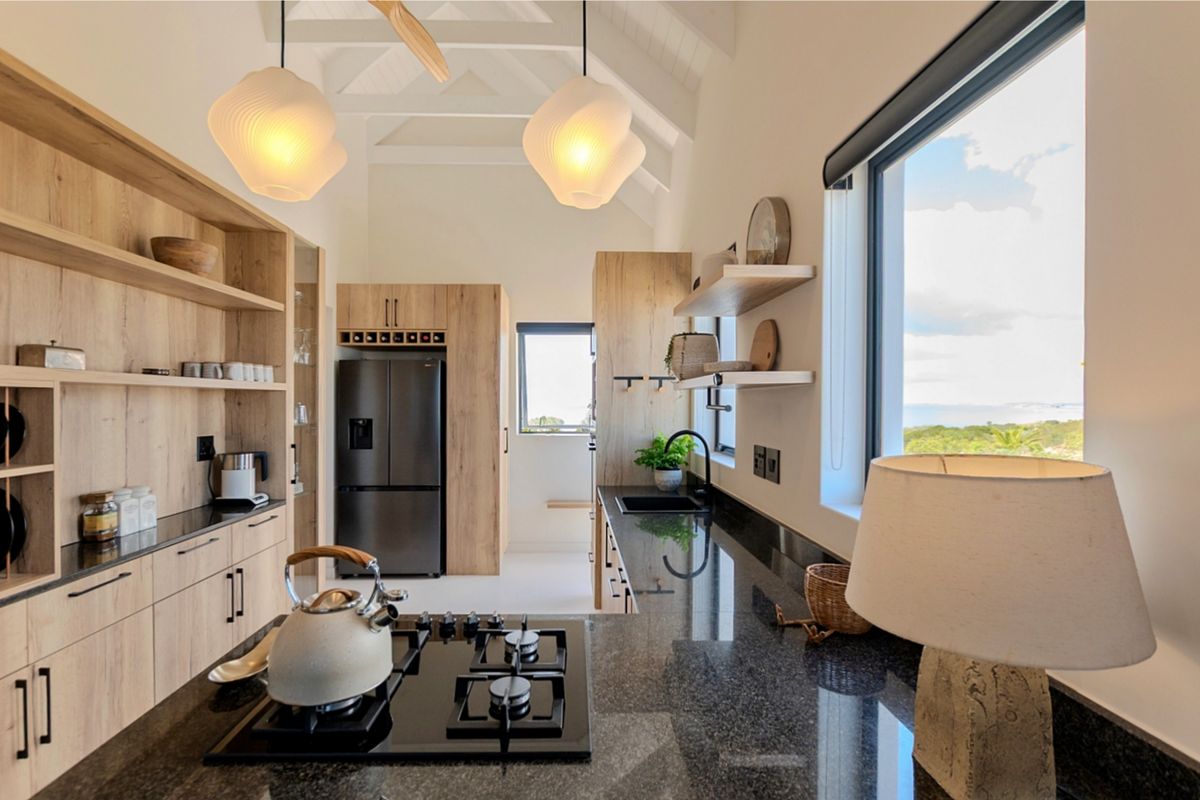 Modern kitchen featuring light wood cabinetry, dark granite countertops, a gas hob, and vaulted ceilings with exposed rafters, offering a bright and functional workspace.