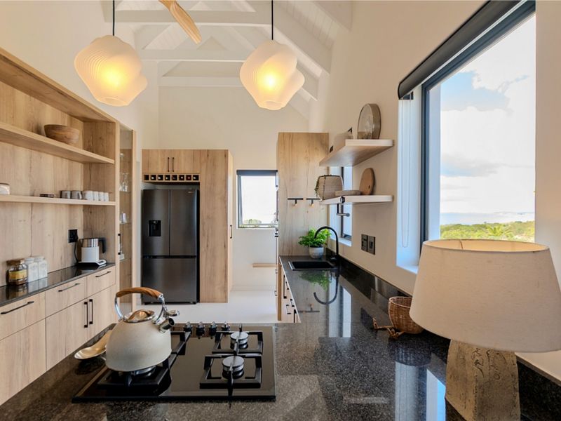 Modern kitchen featuring light wood cabinetry, dark granite countertops, a gas hob, and vaulted ceilings with exposed rafters, offering a bright and functional workspace.