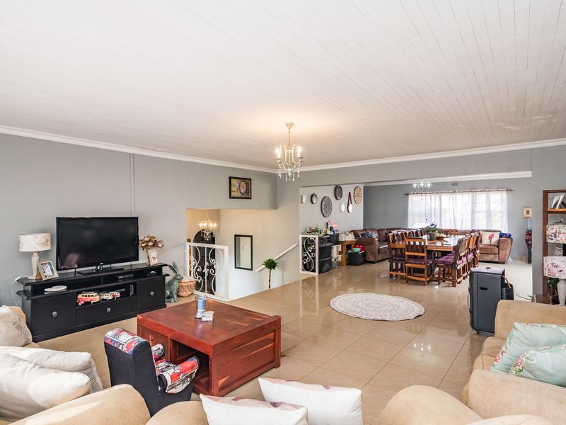 Spacious open-plan living and dining area featuring polished tiled floors, a classic tongue and groove ceiling, and an elegant wrought iron staircase railing.