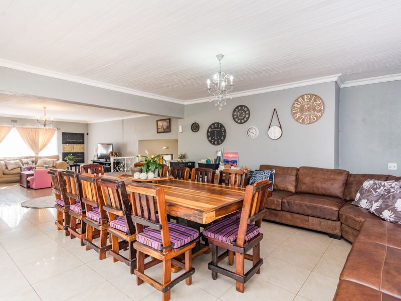 Spacious open-plan living and dining area featuring tiled flooring, a classic tongue and groove ceiling, and elegant chandelier lighting.