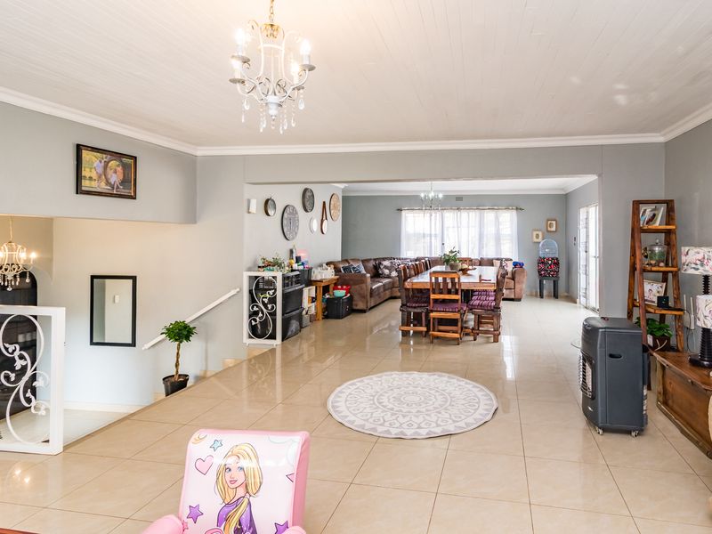Spacious open-plan living and dining area featuring large format floor tiles, decorative ceiling finishes, and a classic wrought iron staircase balustrade.