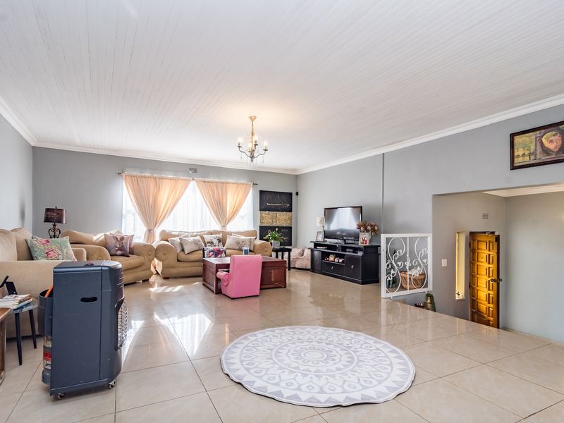 Spacious living room featuring large format floor tiles, a white tongue and groove ceiling, and a decorative metal balustrade overlooking a recessed staircase.