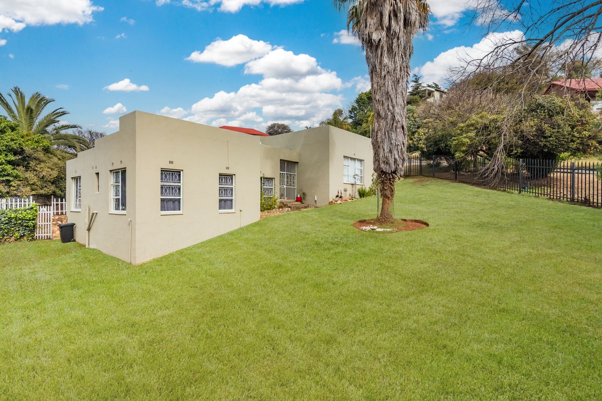 Rear view of the house featuring a large lawn, security bars on windows, and perimeter metal fencing.