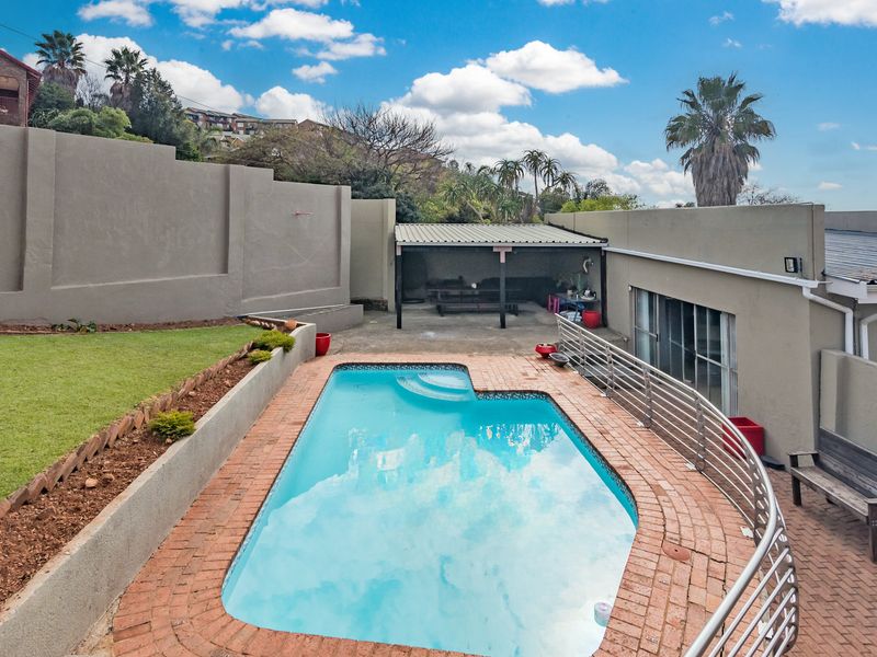 Outdoor pool area featuring a swimming pool with brick paving, a retaining wall, and a covered patio space.