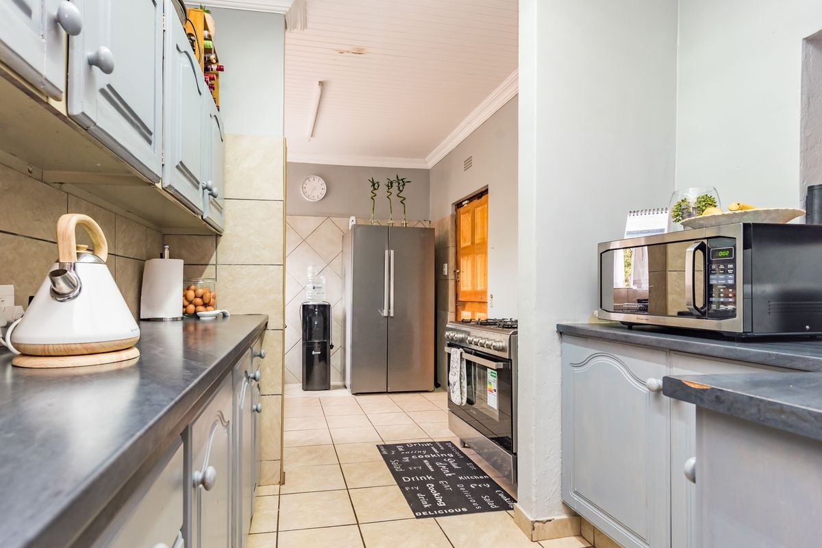 A functional galley-style kitchen featuring light grey cabinetry, dark countertops, tiled flooring, and a built-in gas stove.