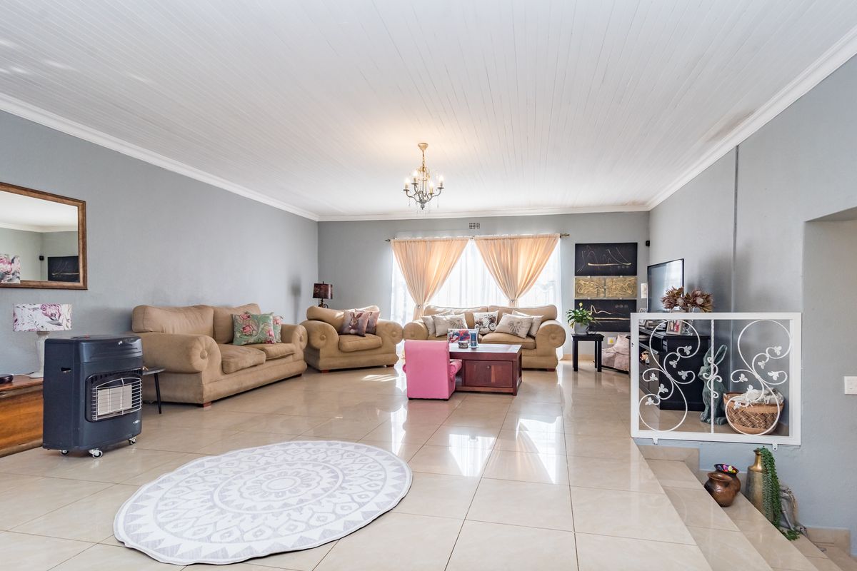 Spacious living room featuring large format floor tiles, a classic tongue and groove ceiling, and a decorative metal balustrade overlooking a lower level.