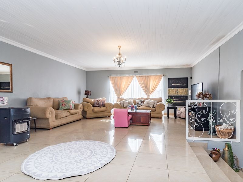 Spacious living room featuring large format floor tiles, a classic tongue and groove ceiling, and a decorative metal balustrade overlooking a lower level.