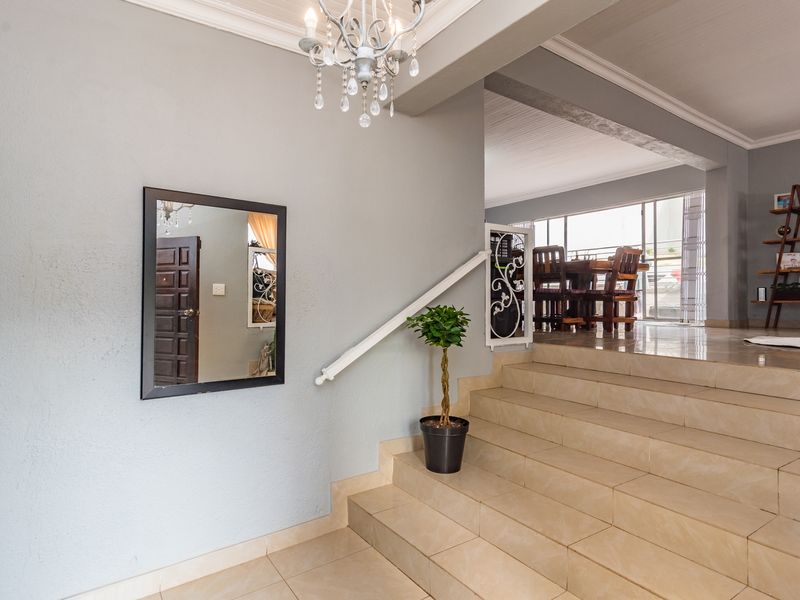 Welcoming entrance hall featuring a tiled staircase with a decorative wrought iron balustrade, leading into an open-plan living area.